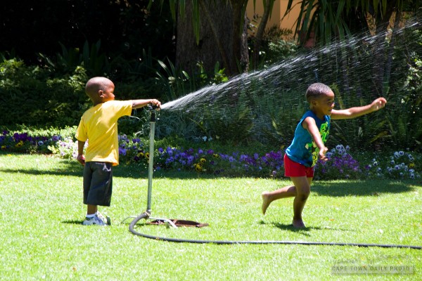 A kid, a sprinkler, and a really wet sibling