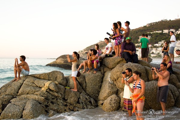 People sitting on a rock, taking a photo of the sunset